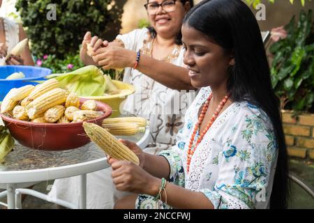 Zwei Frauen, die im Garten kochen. Sie schälen Mais. Einheimisches Speisenkonzept. Stockfoto