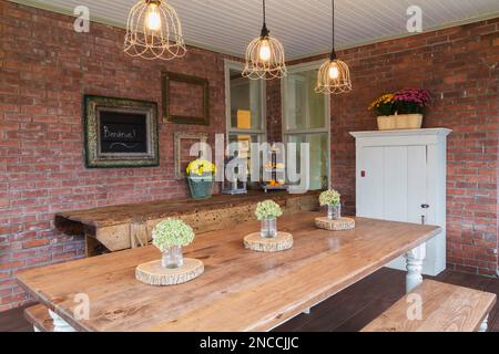 Pinienholztisch und Sitzbänke, alte Werkstattbank und weiße Holzschränke auf der Veranda hinter dem alten viktorianischen Queen Anne Revival-Haus aus dem Jahr 1900. Stockfoto