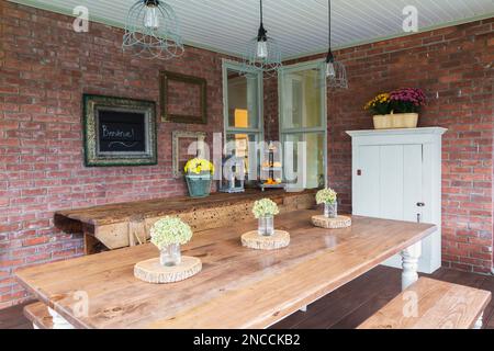 Pinienholztisch und Sitzbänke, alte Werkstattbank und weiße Holzschränke auf der Veranda hinter dem alten viktorianischen Queen Anne Revival-Haus aus dem Jahr 1900. Stockfoto