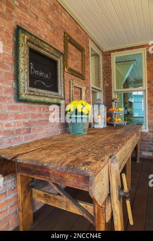 Alte gebrauchte und abgenutzte rustikale hölzerne Werkstattbank auf der Veranda hinter dem alten viktorianischen Queen Anne Haus im Revival Stil von 1900. Stockfoto