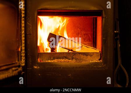 Nahaufnahme von Holzstämmen, die in einem Holzfeuer brennen, mit offener Tür im Wohnzimmer. Stockfoto