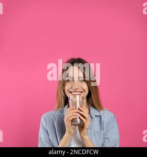 Junge Frau trinkt Schokoladenmilch auf rosa Hintergrund Stockfoto