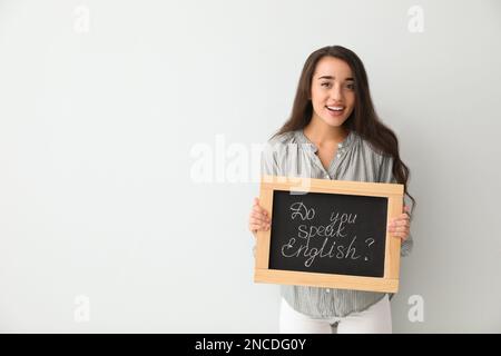Junge Lehrerin mit Tafel und Wörtern Sprechen sie Englisch? Auf hellem Hintergrund. Platz für Text Stockfoto
