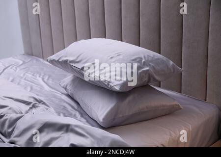 Gemütliches Bett mit weicher seidiger Bettwäsche in hellen Zimmern Stockfoto