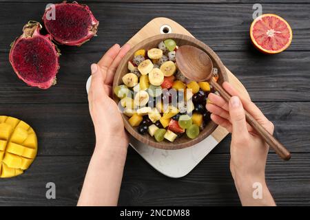 Frau mit köstlichem exotischen Obstsalat am schwarzen Holztisch, Draufsicht Stockfoto