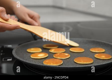 Eine Frau dreht Cornflakes-Pfannkuchen mit Pfannenwender auf dem Herd, Nahaufnahme Stockfoto