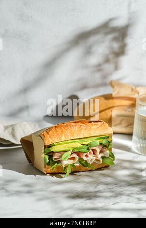 Avocado und parma Sandwich. Baguette-Sandwich in handwerklicher Verpackung für die Lieferung Stockfoto