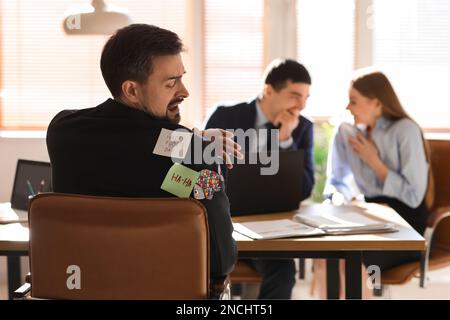 Haftnotizen auf der Rückseite eines jungen Mannes, der im Büro sitzt. Feier zum 1. April Stockfoto