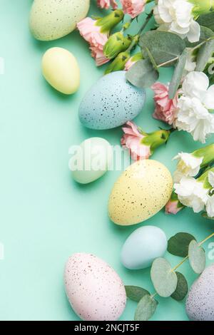 Osterfarbene Eier und ein Strauß weißer und rosafarbener Nelken mit Eukalyptuszweigen auf einem weichen grünen Hintergrund. Festlicher Hintergrund. Stockfoto