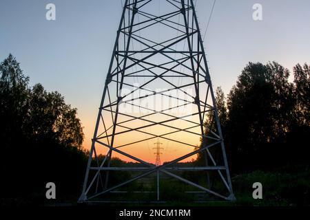 Der Endanker unterstützt Überlandleitungen mit Drähten am Horizont bei einem hellen Sonnenuntergang im Wald durch Metallstangen und -Stangen, Rahmen. Stockfoto