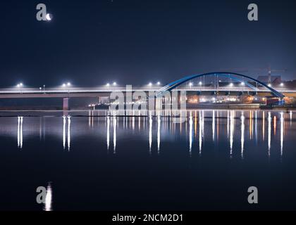 Slubice, Polen. 15. Februar 2023. Der schwindende Mond scheint am frühen Morgenhimmel über der hell erleuchteten Stadtbrücke über der deutsch-polnischen Grenze (oder). Die Brücke verbindet Slubice in Polen am linken Ufer mit Frankfurt (oder) in Brandenburg. Kredit: Patrick Pleul/dpa/Alamy Live News Stockfoto