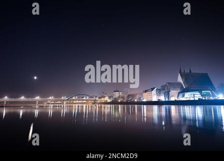 Slubice, Polen. 15. Februar 2023. Der schwindende Mond scheint am frühen Morgenhimmel über der hell erleuchteten Stadtbrücke über der deutsch-polnischen Grenze (oder). Die Brücke verbindet Slubice in Polen am linken Ufer mit Frankfurt (oder) in Brandenburg. Kredit: Patrick Pleul/dpa/Alamy Live News Stockfoto