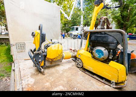 Der kleine Plattenverdichter, der stehende Vibrationshammer und die Stützmaschine wurden auf den Lkw-Anhänger gestellt. Elektrowerkzeuge auf der Baustelle. Stockfoto