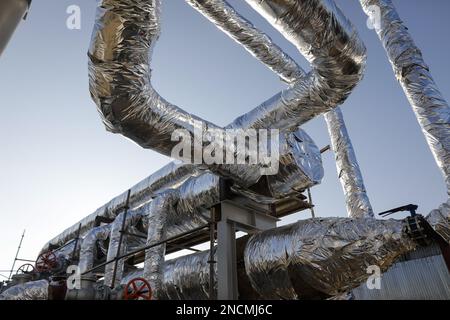 Details zu industriellen metallischen Rohrleitungen, die mit Zinnfolie bedeckt sind und durch die heißes Wasser fließt. Stockfoto