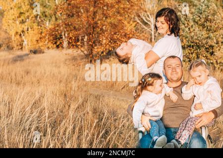 Familie mit Drillingen auf einem Spaziergang. Glückliche Eltern halten Kinder draußen in den Armen Stockfoto