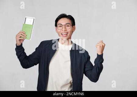 Aufgeregter Reisender, asiatischer Tourist, der Bordkarten für Reisepässe besitzt und eine Siegergeste macht Stockfoto