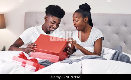 Ich habe das auf deiner Wunschliste gesehen. Ein junger Mann verwöhnt seine Freundin mit Geschenken in ihrem Schlafzimmer. Stockfoto