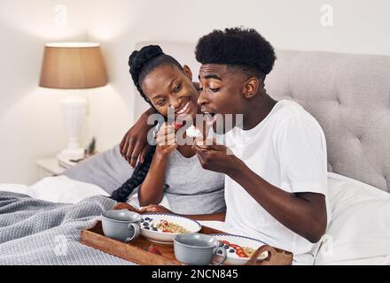Ich genieße ein schuldfreies Frühstück. Ein glückliches junges Paar, das zusammen im Bett frühstückt. Stockfoto