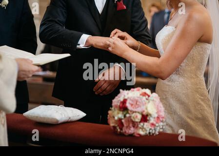 Eine Braut in einem weißen Kleid zieht während der Hochzeitszeremonie einen Ring für den Bräutigam an Stockfoto