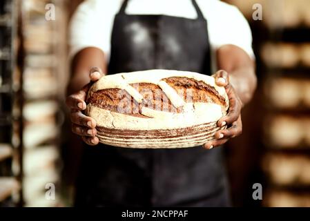 Du wirst wieder kommen. Ein männlicher Bäcker, der einen frisch gebackenen Brotlaib in der Hand hält. Stockfoto