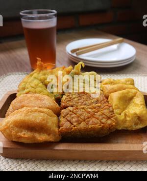 Nahaufnahme von gebratenem Tofu, gebratenem Tempeh, gebratenen Kartoffelkuchen und Cornflakes auf einem Holztablett Stockfoto