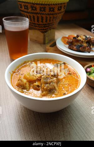 Eine Schüssel Rindfleisch-Curry mit Karotten, serviert mit einem Glas Tee auf einem Holztisch Stockfoto