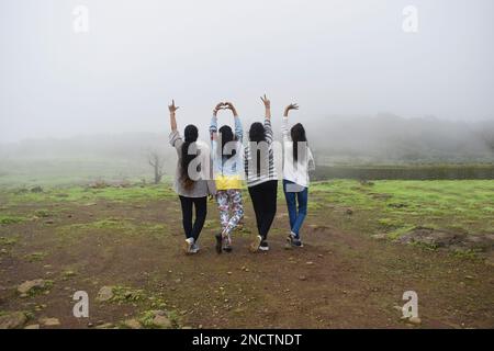 MAHARARSHTRA, PUNE, LONAVALA, 2022. August, Gruppe indischer Teenager-Mädchen in farbenfrohen, lässigen Outfits, die die Natur genießen, mit Blick auf die Rückseite zeigt Hand si Stockfoto