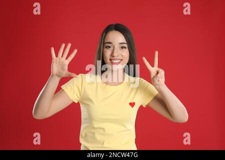 Eine Frau in einem gelben T-Shirt, die Nummer sieben zeigt, mit ihren Händen auf rotem Hintergrund Stockfoto