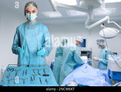 Krankenschwester in Tischnähe mit verschiedenen chirurgischen Instrumenten im Operationssaal Stockfoto