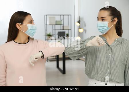 Frauen grüßen sich gegenseitig, indem sie sich im Büro mit Ellbogen statt Handschlag anstoßen Stockfoto