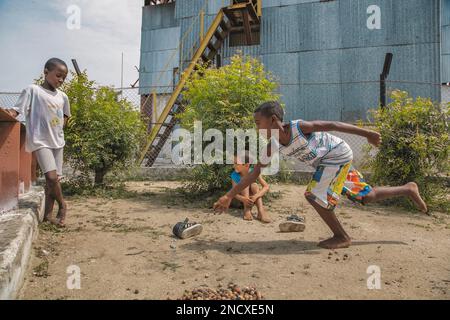Augusto César Sandino, Artemisa, Kuba. 12. Juli 2019. Zwei schwarze Jungs und ein weißer Junge, die barfuß im Dreck mit trockenen Samen Murmeln spielen, in Kuba. Stockfoto