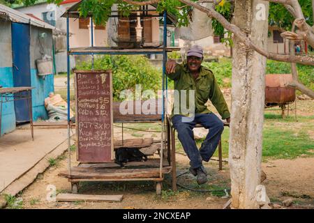 Augusto César Sandino, Artemisa, Kuba. 11. Juli 2019. Älterer schwarzer Bauer, der neben seinem leeren Gemüsestand sitzt und in die Kamera lächelt. Stockfoto