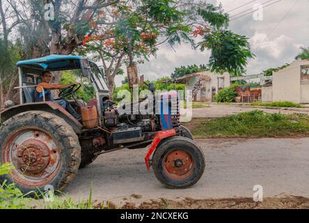 Augusto César Sandino, Artemisa, Kuba. 11. Juli 2019. Ein Bauer, der einen Traktor auf einer Straße mit einem zerstörten Gebäude im Hintergrund in einer Landstadt fährt. Stockfoto