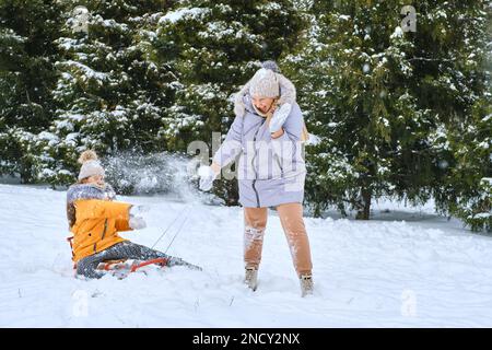 Wintermärchen, glückliche Mutter, die mit einem Mädchen Schlitten zieht, auf einer verschneiten Parkstraße im tiefsten, frischen Schnee. Genießen Sie den weißen Wintertag. Zeit miteinander verbringen Stockfoto