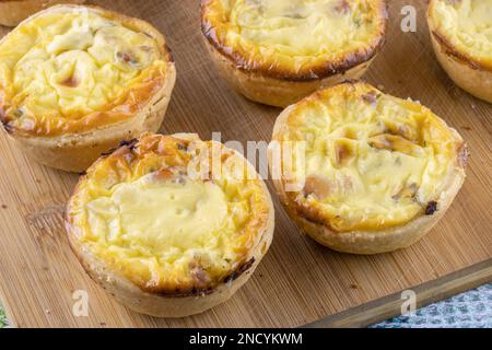 Käsige Vorspeise, Mini-Quiches, hausgemacht auf hölzernem Küchenbrett, Nahaufnahme Stockfoto