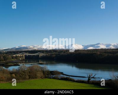 Blick über die Menai Strait Thomas Telfords Hängebrücke in Richtung der schneebedeckten Carnedd Mountains im Snowdonia Nationalpark Menai Bridge Anglesey Stockfoto