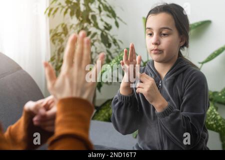 Kleines, kaukasisches Teenager-Kind Machen Sie zu Hause Artikulationsübungen mit einer fürsorglichen Mutter oder einer fürsorglichen Lehrerin. Das kleine Kind spricht Geräusche aus, spricht mit dem Lehrer oder Stockfoto