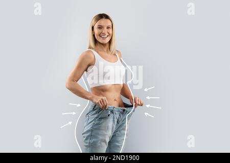 Fröhliche, schlanke blonde Frau in riesigen Jeans Stockfoto