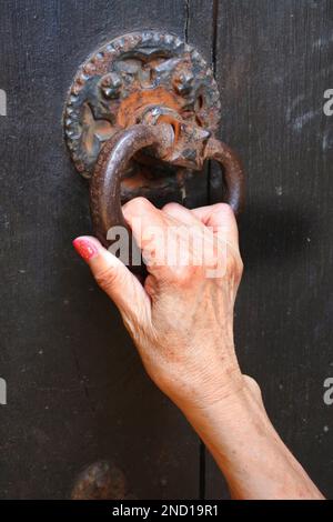 Weibliche Hand klopft an einen rostigen alten Türklopfer - John Gollop Stockfoto