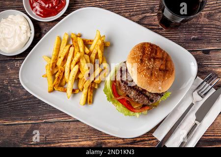 Köstlicher gegrillter hausgemachter Hamburger mit Rind, Tomaten, Käse und Salat auf rustikalem Holzhintergrund Stockfoto