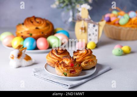 Craffin mini (Cruffin) mit Rosinen und kandierten Früchten. Traditionelles Osterbrot Kulich. Im Hintergrund ist ein großes Cruffin und bemalte Eier auf einem gr Stockfoto