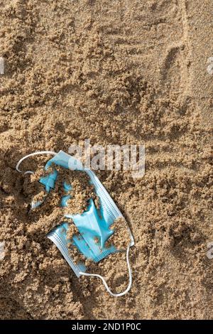 Weggeworfene chirurgische medizinische Gesichtsmaske liegt im Sand am Strand, Nahaufnahme, gekürzt, vertikaler Schuss Stockfoto