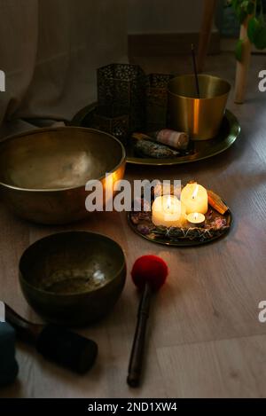 Von oben: Traditionelle tibetische Gesangsschüsseln mit brennenden Kerzen und Aromatherapie-Lampen auf Parkettboden Stockfoto