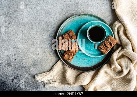 Von oben Keramikplatte mit frisch gebackenen Schokoladenkeksen in der Nähe eines schwarzen Kaffeegetränks in einer Tasse auf Betonhintergrund Stockfoto