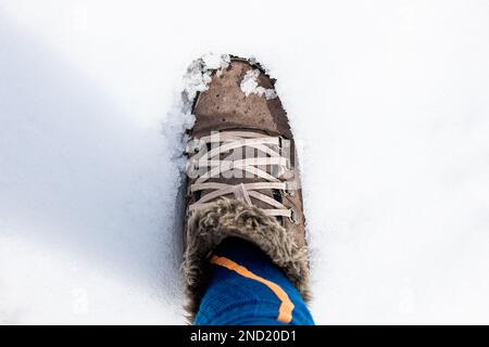 Draufsicht einer unbekannten Person in warmen Stiefeln, die im Winter auf verschneitem Boden steht Stockfoto