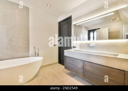 Ovale weiße Keramikbadewanne im geräumigen kreativen Badezimmer mit Holzmöbeln im modernen Haus Stockfoto