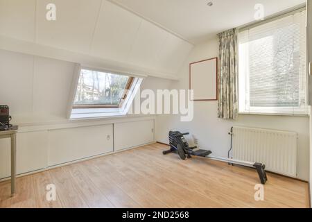 Heller, moderner Raum mit Trainingsausrüstung und Fenstern mit Vorhängen in der Nähe eines an der weißen Wand hängenden Bilderrahmens Stockfoto