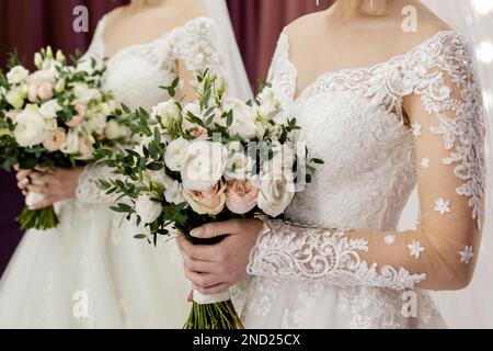 Die Braut in einem weißen Hochzeitskleid hält ihren Brautstrauß in den Händen Stockfoto