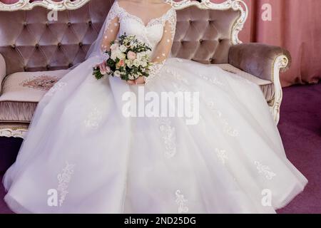 Die Braut in einem weißen Hochzeitskleid hält ihren Brautstrauß in den Händen Stockfoto