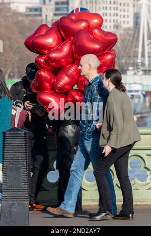 Westminster Bridge, London, Großbritannien. 15. Februar 2023. Der Tag ist seit einem kühlen Morgengrauen sonnig, hat sich aber in der Stadt auf etwa 14 Grad Celsius erwärmt. Person, die Herzballons nach Valentinstag verkauft Stockfoto